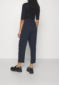 Marina tapered byxor med hög midja, slät textur och sidofickor. I kombination med kraftiga svarta loafers med en strukturerad sula.