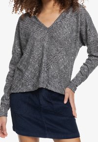 Suéter de punto gris con escote en V, patrón texturizado y corte holgado. Combinado con una falda de pana azul marino con bolsillos delanteros y líneas verticales.