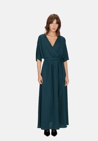 Lange wikkeljurk in diep teal stof met een V-hals en korte mouwen. Heeft een gestrikt taille en een vloeiende, lange rok.