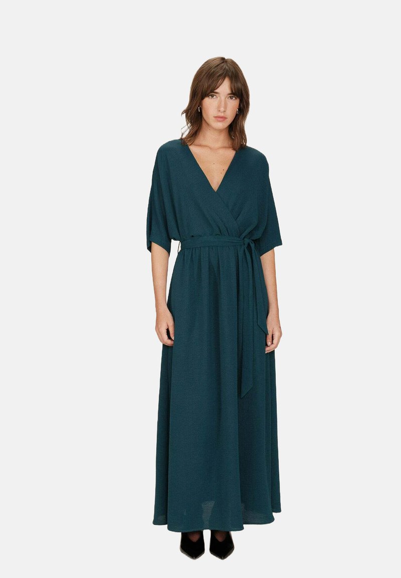 Lange wikkeljurk in diep teal stof met een V-hals en korte mouwen. Heeft een gestrikt taille en een vloeiende, lange rok.