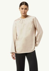 Helles rosa Satinbluse mit Rundhalsausschnitt, gepflegtem Detail und langen Ärmeln, kombiniert mit schwarzen Hosen. Glatte Textur, elegantes Design.