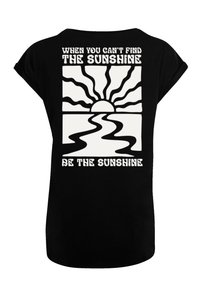 Black t-shirt featuring a white graphic of a sun and wavy lines, with the text “When you can't find the sunshine, be the sunshine” on the back.