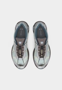 Par športnih copat sive in svetlo modre barve s črnim sistemom hitrega vezanja, pogled iz zraka na belem ozadju.