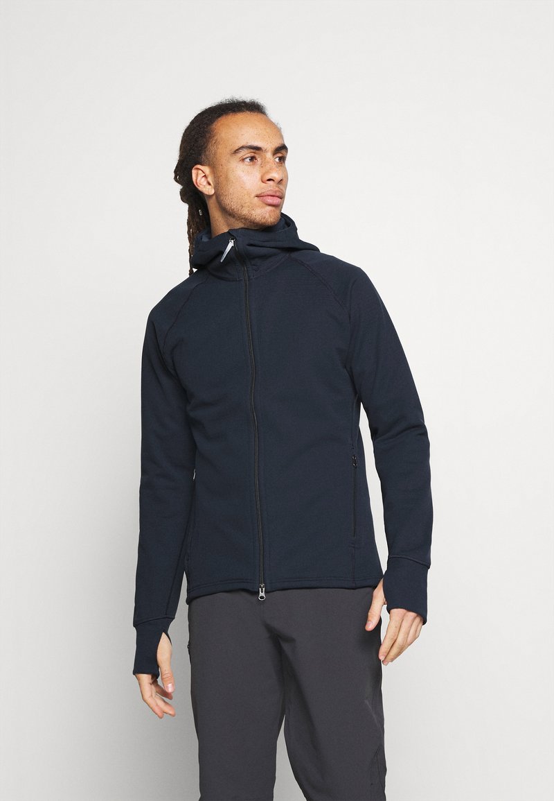 Navy Zip-Up-Jacke mit Kapuze, gefertigt aus einem strukturierten, flexiblen Stoff. Verfügt über Daumenlöcher an den Bündchen und seitliche Taschen zur Aufbewahrung.