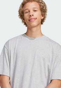 Grå bomulls t-shirt med kort ärm och rund halsringning, med en subtil grön kant vid kragen. Mjuk textur och avslappnad passform.