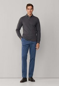 Polo à manches longues gris foncé, pantalon bleu clair, chaussures marron. Le polo est doté d'un col avec trois boutons et d'un tissu texturé.