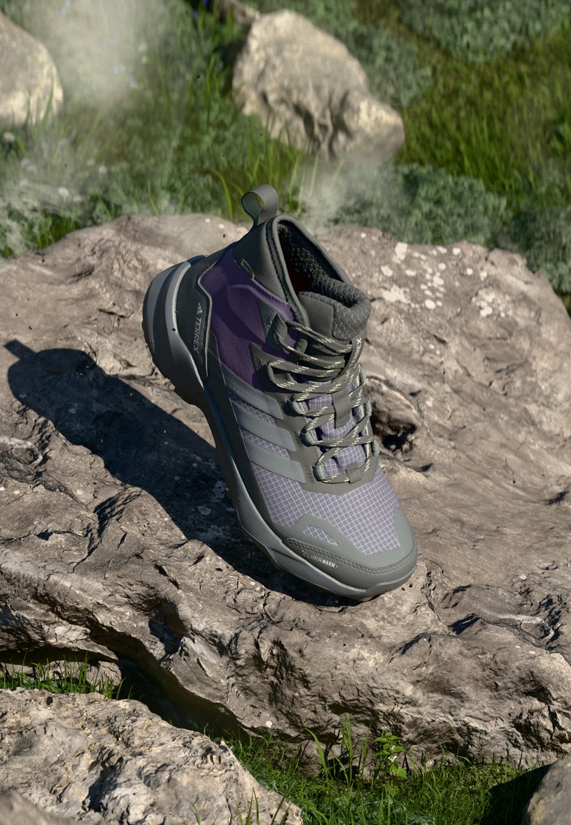 Gray and purple hiking boot with textured mesh upper, lacing system, and rubber sole, positioned on a rocky surface with grass.