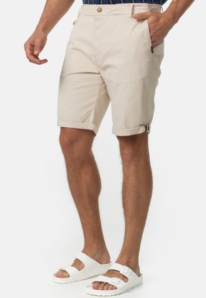 Man wearing beige rolled-up shorts, a navy striped shirt, and white buckle sandals against a plain background.