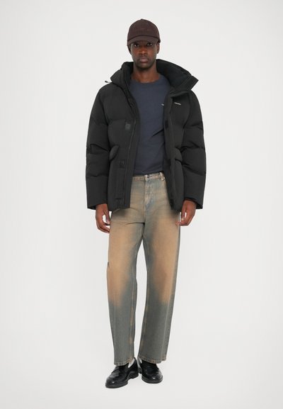 A black puffer jacket with a zippered front and elastic cuffs, paired with faded loose-fit jeans. Black shoes complete the outfit.