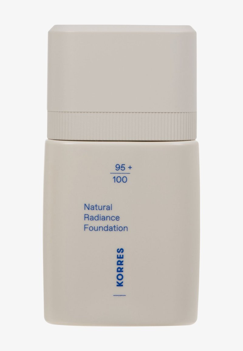 Base de maquillaje natural Korres con radiancia, en un envase beige mate con tapa acanalada. Presenta texto azul que indica los tonos 95 y 100.