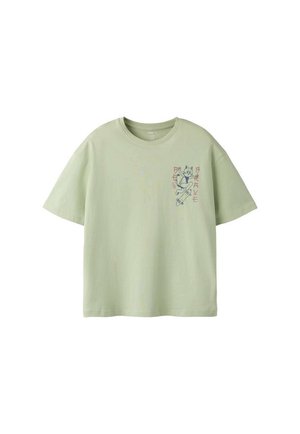T-shirt vert clair à manches courtes avec un petit dessin d'un chat en train de faire du skate et le mot « BRAVE » en lettres stylisées sur la poitrine.