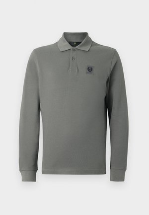 Long-sleeve polo shirt in olive green, made from textured fabric, featuring a three-button placket and a logo patch on the chest.