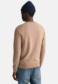 Hellbraunes gestricktes Sweatshirt mit Rundhalsausschnitt, langen Ärmeln und gerippten Bündchen, getragen mit blauen Jeans und einer marineblauen Mütze. Einfaches Design.