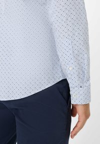 Lichtblauw button-up shirt met een klein bladmotief, met lange mouwen en manchetknoopjes, gecombineerd met donker marineblauwe broek.