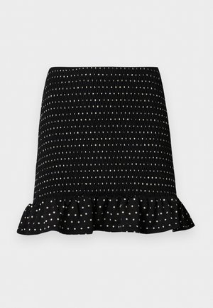 Mini fustă neagră cu buline albe, textură smock și tiv cu volane, pe un fundal simplu, deschis la culoare.
