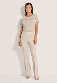 Beige gebreide top met korte mouwen, voorzien van horizontale uitsnijdingen, gecombineerd met lichtbeige aansluitende broek met verticale naden.