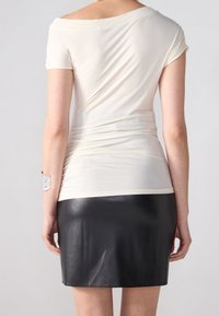 Krämfärgad off-shoulder topp med korta ärmar, lager av textur. Svart läder mini kjol med en slät, glänsande yta och en elegant silhuett.