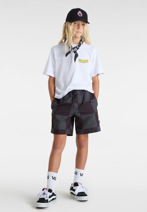 Camiseta blanca con el logo amarillo de "VANS", pantalones cortos a cuadros en negro, gorra negra y zapatillas en blanco y negro con calcetines blancos.