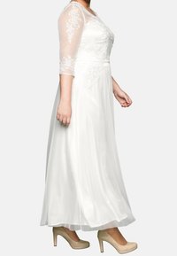 Vit lång klänning med genomskinliga ärmar i armbågs-längd, blommig broderi på livstycket, flödande kjol, kombinerad med nude-hälar.