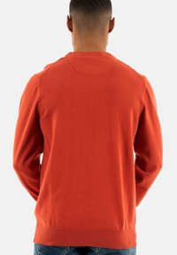 Pull en maille orange avec un col rond, des poignets et un ourlet côtelés. Vue de dos montrant une texture lisse et un design simple.
