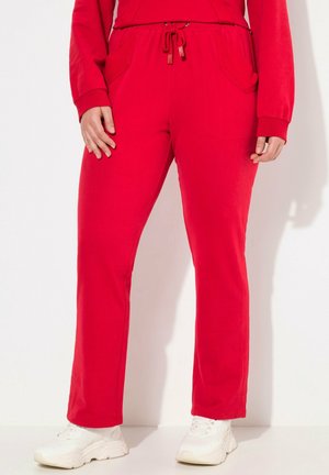 Persoon draagt felrode sweatpants met zijzakken en een aantrekkoord in de taille, gecombineerd met witte chunky sneakers, staand tegen een witte achtergrond.