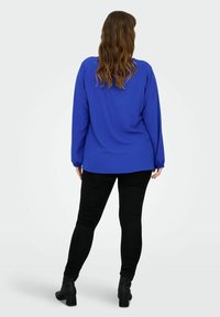 Blaues Langarmshirt mit lockerer Passform, runder Saum und elastischen Manschetten, kombiniert mit schwarzen Leggings und Ankle Boots.