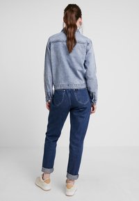 Jasnoniebieska dżinsowa kurtka z długimi rękawami, krótki fason i zapięcie na guziki. Zestawiona z ciemnoniebieskimi dżinsami, podwiniętymi mankietami i białymi trampkami.