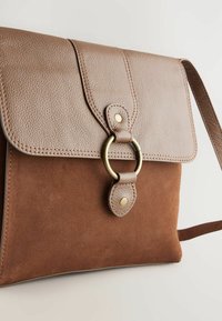Sac en cuir et en daim marron avec un rabat texturé, une fermeture en forme d'anneau doré et une longue sangle réglable. Présente des matériaux et des couleurs contrastants.