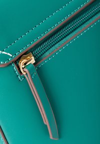 Türkisfarbene synthetische Lederhandtasche mit einem goldenen Reißverschluss, kontrastierenden braunen Akzenten und feinen weißen Nähten entlang der Kanten, die eine qualitativ hochwertige Verarbeitung demonstrieren.