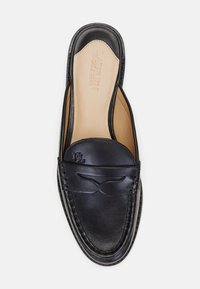 Mocassins pretos em couro com um acabamento liso, apresentando uma costura elevada e um logótipo em relevo. Design de abertura atrás, com uma palmilha bege.