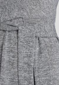 Grå stickad klänning med en texturerad tyg, ett brett bälte och en omslagdesign, med varierande nyanser av grått.