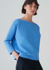 Blauwe textuur trui met horizontale ribbels, ronde halslijn en lange mouwen, gecombineerd met zwarte broek. Glad stofafwerking.