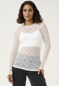 Hvid langærmet top lavet af gennemsigtig blonder med et tekstureret design, der har et solidt hvidt underlag og en tætsiddende pasform.