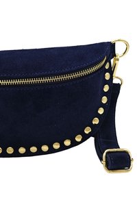 Sac en daim bleu marine avec fermeture éclair dorée et clous le long du bord, forme courbée, bandoulière ajustable et texture lisse.