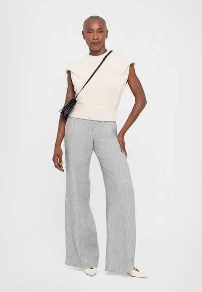 Knitted cream sleeveless top with shoulder detailing, paired with gray vertical striped wide-leg trousers and white pointed-toe shoes. Black handbag.