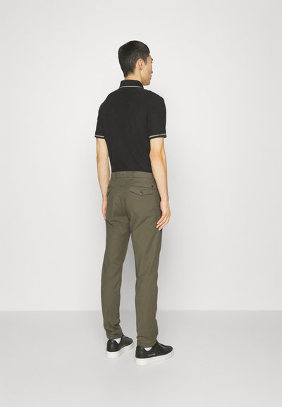 Black polo shirt with contrasting collar and sleeve trim, paired with olive green tapered pants and black sneakers with white soles.