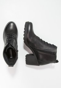 Botas de tobillo de cuero negro con tacón ancho, con diseño de cordones, cremallera en un lado y suela de goma texturizada. Acabado suave.