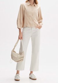 Beige overhemd met knopen en twee borstzakken, witte hoge taille broek, beige schoudertas en witte sneakers met bruine zolen.