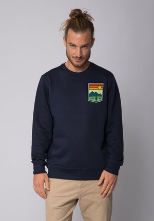 Donkerblauwe sweatshirt van zachte stof, met een voorzijde graphic van bergen, zon en de tekst "GOOD VIBE" in geel en groen.