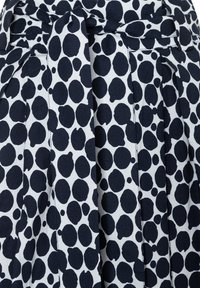 White fabric with large navy blue polka dots, featuring a pleated design and fabric belt at the waist. Smooth texture with a casual appearance.