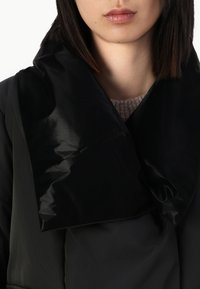 Black puffer coat with a shiny, large collar; textured fabric; close-up view of neckline and face; subtle stitching detail.