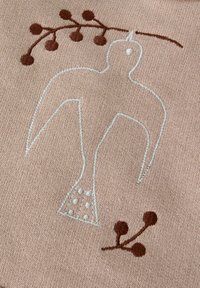 Beżowa tkanina z haftowanym wzorem ptaka w jasnoniebieskim i brązowym kolorze, zawierająca roślinne akcenty oraz kropkowane detale na ciele ptaka.