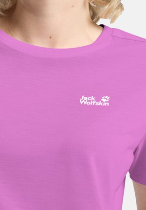 Close-up van een persoon die een paarse Jack Wolfskin T-shirt met een ronde hals draagt, met het merklogo op de borst zichtbaar.