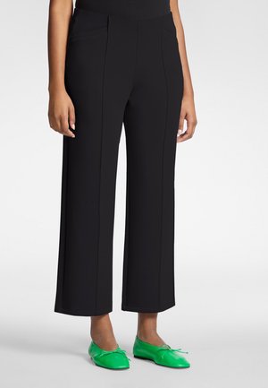 Schwarze Hosen mit weitem Bein, vorderseitigen Nahtdetails und glatter Textur, kombiniert mit leuchtend grünen Ballerinas mit Schleifenakzenten.