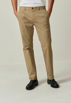 Beige trousers made from lightweight fabric, tailored fit, featuring a button closure and side pockets, paired with black dress shoes.