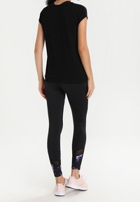 Zwarte top met korte mouwen gecombineerd met zwarte leggings met een kleurblokpaarse accent aan de onderkant en gaasdetails. Roze sneakers.