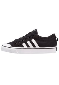 Black canvas sneakers with white rubber toe cap, three white stripes on the side, black laces, and a white sole with textured grip pattern.