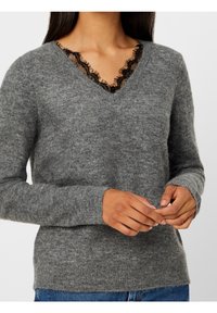 Grauer Strickpullover mit V-Ausschnitt und schwarzer Spitzenverzierung. Lange Ärmel mit gerippten Bündchen, weiche Textur und angenehmer Sitz.