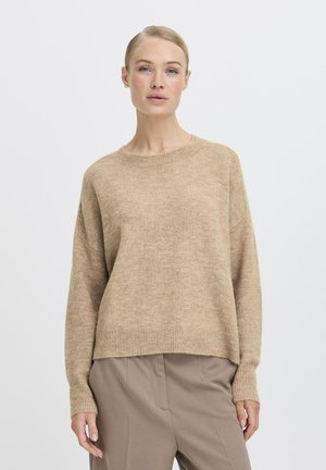 Maglione a maglia beige con collo rotondo e polsini a costine, caratterizzato da una vestibilità rilassata e una texture morbida, abbinato a pantaloni beige su misura.