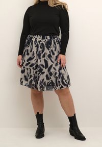 Haut à manches longues noir côtelé associé à une jupe grise à volants ornée d'un motif abstrait bleu marine et noir. Porté avec des bottines noires.